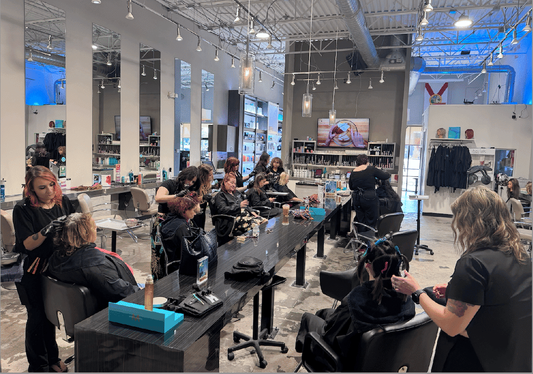 Salon interior with stylists working on clients, mirrors and shelves in view.